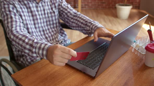 Disabled Man Sitting Wheelchair Front of Laptop with Bank Card in His Hand Filling Out Information