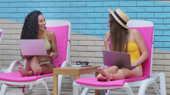 Two Happy Young Multiracial Caucasian Hispanic Women Freelancers Sitting on Sun Lounger Relaxing at