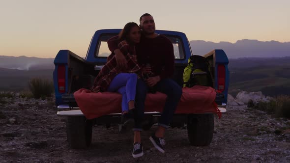 Young couple on a road trip sitting outside on their truck at dusk