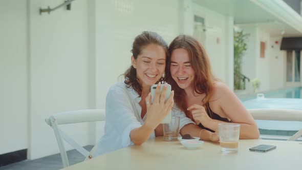 Two Young Attractive Women Drinking Coffee at a Restaurant and Looking at Phone