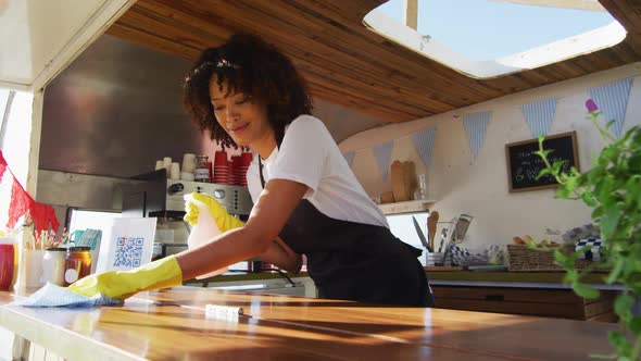 African american woman wearing apron and gloves cleaning the food truck with disinfectant spray