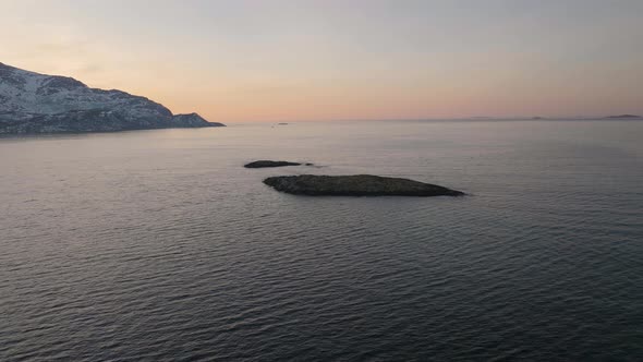 Aerial drone orbits small rocky island, Tromvik Kvaloya Northern Norway sunset