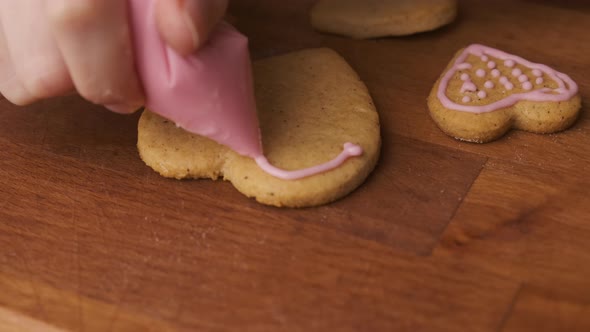 Decorating Gingerbread Cookies or Biscuits in the Shape of Heart with Pink Glaze for Valentines Day