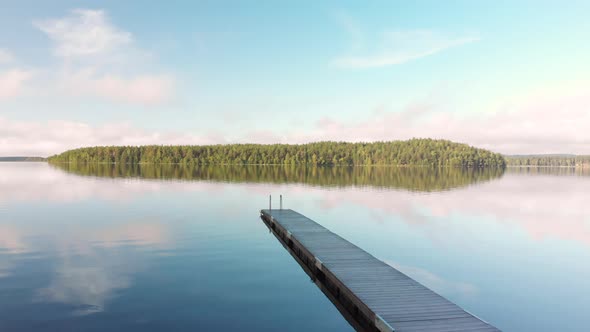 Crane move up above a wooden pier at a calm serene lake watching a small island far away.