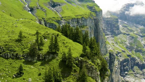 Flying over beautiful, green mountains in Switzerland with a small house located on slope