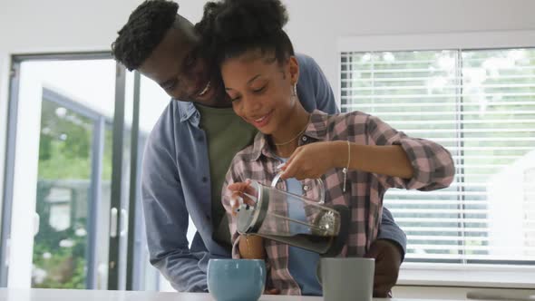 Video of happy african american couple preparing coffee and embracing at home