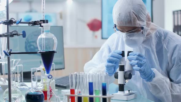 Chemist in Coverall Looking Into a Microscope in High End Laboratory