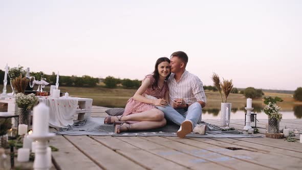 Couple in Love Are Sitting on a Wooden Deck on the Lake. Bridge Arranged with Decoration for