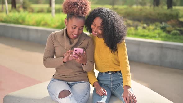 Two young black african women watching something on the phone in the park