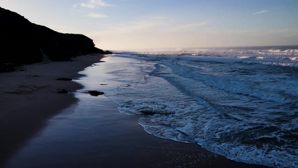 Drone flight revealing sunrise as gentle waves run onto beach, Wilderness, Garden Route