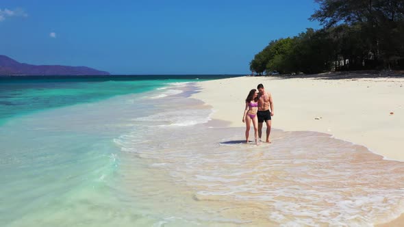 Man and woman suntan on marine resort beach holiday by aqua blue ocean with bright sand background o