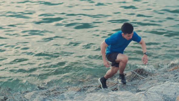 Male runner sprinting trying upon the rock at the seaside.