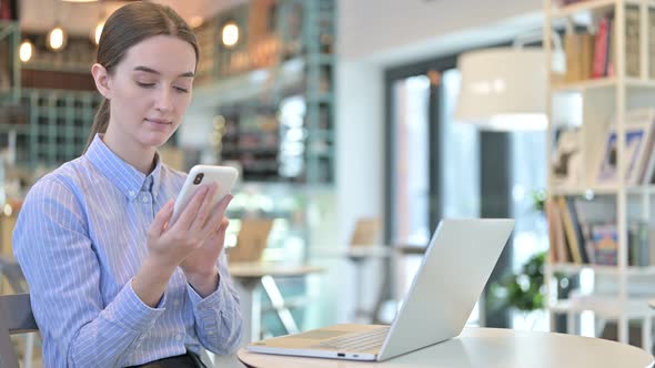 Smartphone Use By Young Businesswoman with Laptop in Cafe