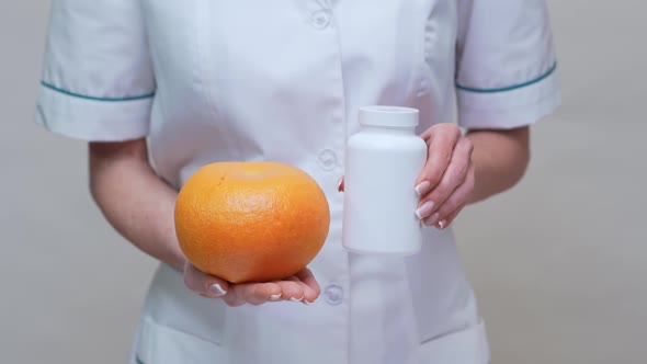 Nutritionist Doctor Healthy Lifestyle Concept - Holding Organic Grapefruit and Jar of Vitamin Pills