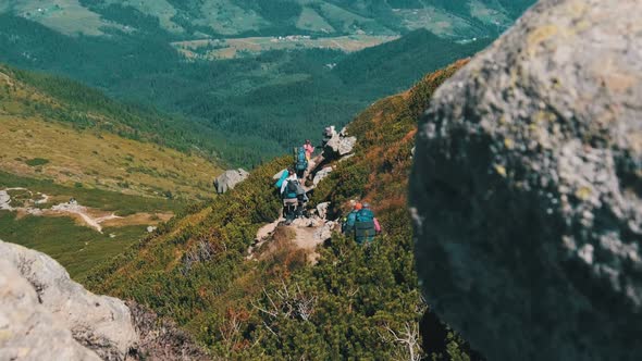 Group of Tourists and Children with Backpacks Go Down on Stone Trail in Mountain