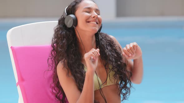 Funky Hispanic Girl Wearing Headphones Dancing Listening Favorite Song Music Podcast in Sun Lounger