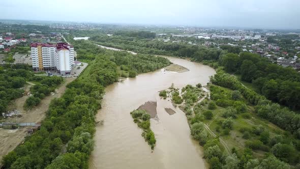 Aerial view of wide dirty river with muddy yellow water flowing through a city in flooding period 