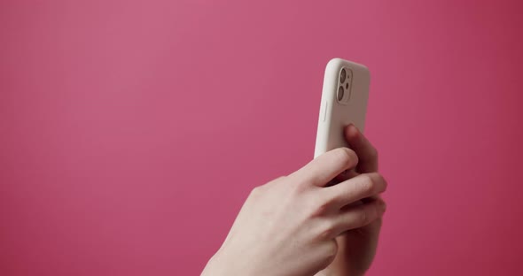 Woman's Hands Use a White SmartPhone on an Isolated Pink Background