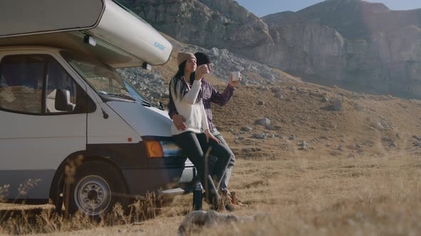 Man and Woman Drinking Coffee and Talking While Traveling By Camper in Countryside Rbbro