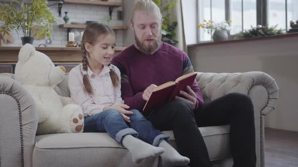 Portrait of Intelligent Young Father Reading To His Lovely Daughter. Interested Teen Girl Listening