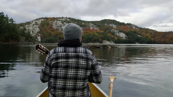 Man plays Guitar in Canoe in Autumn Leaf Color Forest in slow motion on Canada lake. Wide Pan of Fal