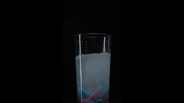 Candy falling into fizzy water closeup in slowmotion