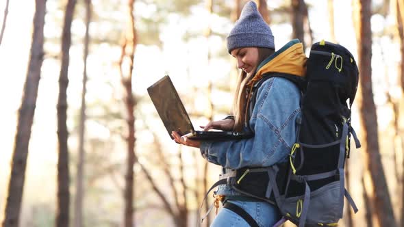 Young attractive girl with a large hiking backpack communicates online with friends using a laptop