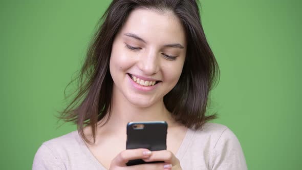 Young Happy Beautiful Woman Smiling While Using Phone Against Green Background