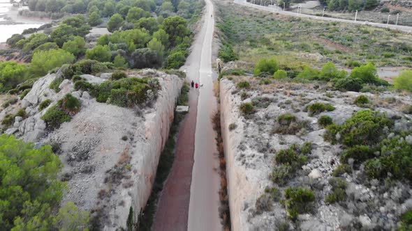 Couple walks with dogs along a path made between a rock cliff and vegetation on the sides