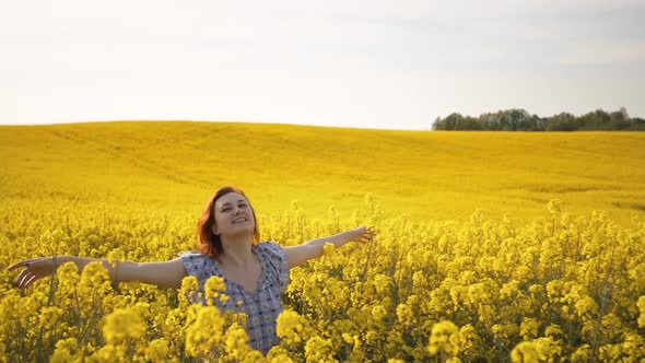 Camera Moves Back: Young Woman Smiles and Enjoys Rapeseed Field Walking Forward