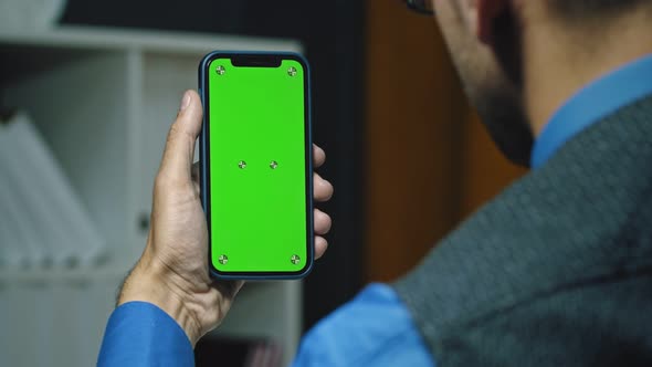 Businessman looks at smartphone green screen.