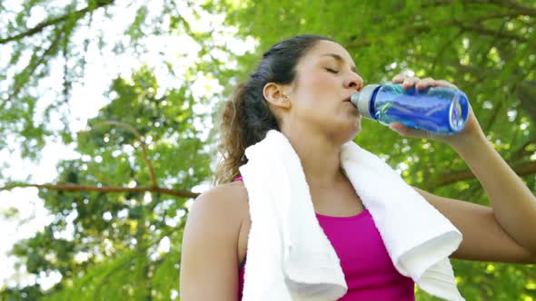Woman wiping her brow and drinking water after workout in the park