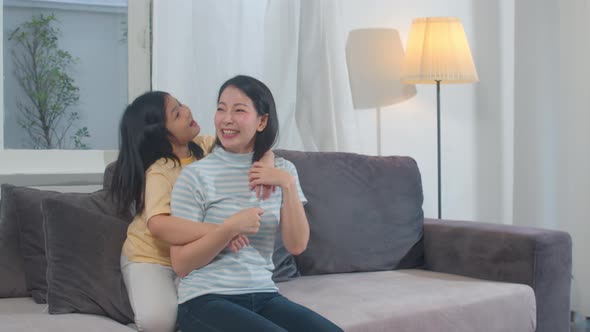 Happy young Asian family mom and kid play together on couch at home.