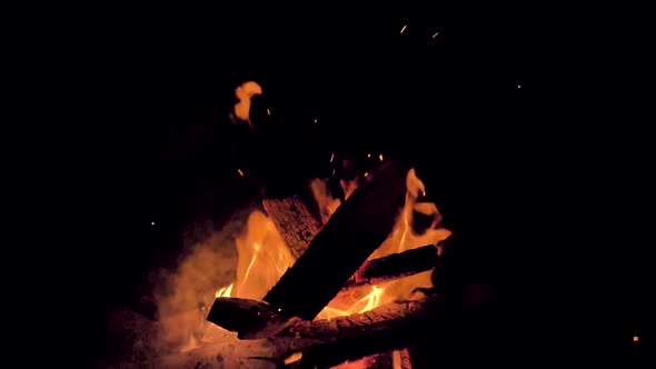 Hot, glowing embers float into the night sky as a bonfire smokes and burns on the beach in the Magda