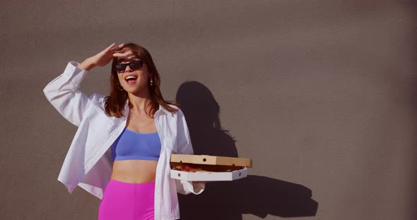 girl holds a pizza in her hands and covers her eyes from the sun with her palm