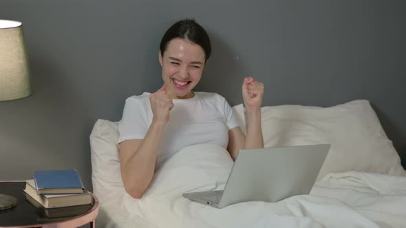 Young Woman Celebrating on Laptop in Bed 