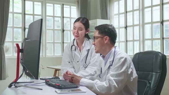 Medical Office: Two Asian Professional Physicians Talking, Consulting And Working On Computer