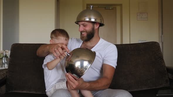 A Father is Playing with His Son with the Lids From the Dishes in the Hotel