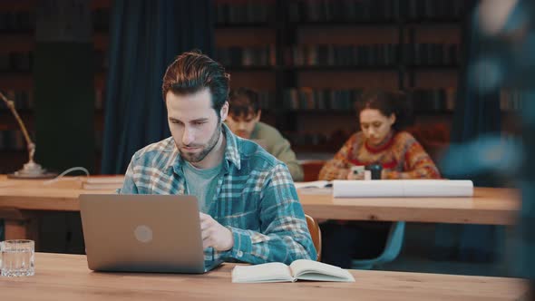 Millennial Male Student Engaged in Work on Laptop at Library