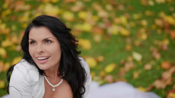 Charming Brunette Woman in Wedding Dress is Smiling Broadly and Posing in Park in Fall Day