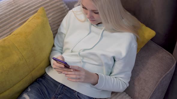 Young female user using mobile phone while sitting on sofa at home.