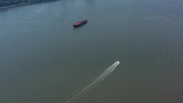 A drone view of a large red barge anchored and a small boat going by in the Hudson River in NY on a