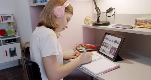 Teenager with Headphones Writes on Notebook and Uses Tablet Gadget for Internet