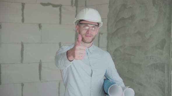 Young engineer-architect with  blueprints looks at the camera and shows like alt