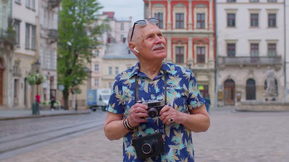 Senior Man Tourist with Retro Photo Camera Smiling Listening Music Earphones Dancing on Street