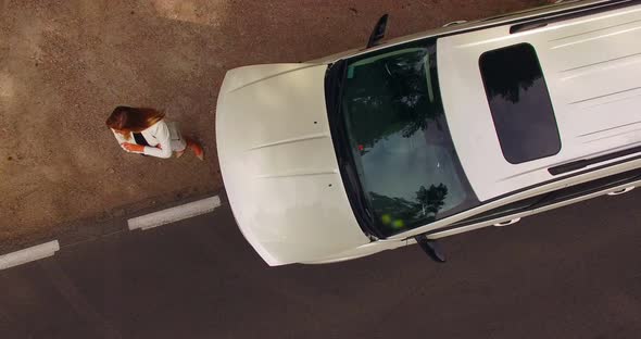 4k aerial shot of a stranded young woman looking under the hood of her broken down car.