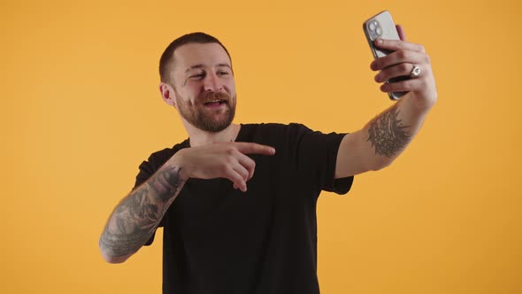 Handsome Bearded Man Taking Video with Smartphone Moving His Arm Isolated Studio Shot Yellow