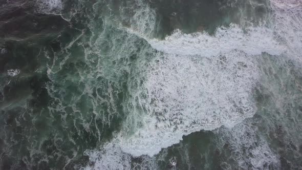 Churning white breaking waves move slowly shoreward, vertical aerial