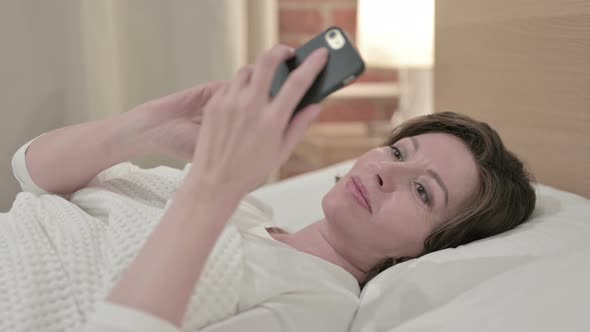 Attractive Old Woman Using Smartphone in Bed 