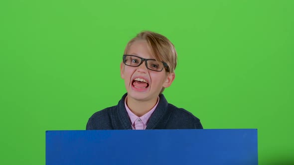 Child Boy in the Glasses Looks Out From Behind a Board and the Curves of the Face on the Green